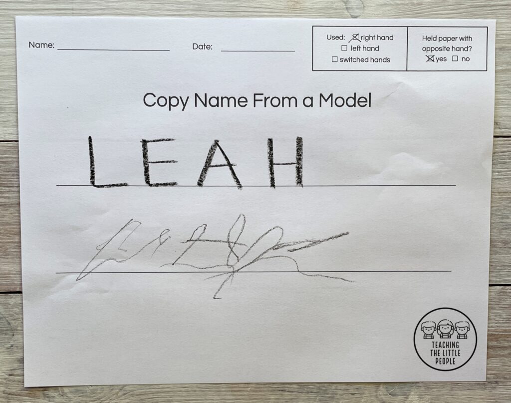 Adult writing of word "Leah" on a line, with a child's scribbling attempt at imitating on line below.